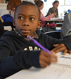 Tito Ekundat, a refugee student from the Congo, takes notes with his fifth grade class