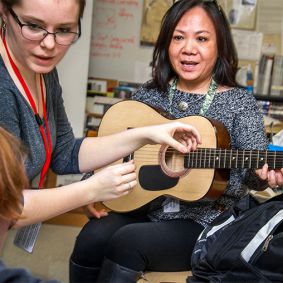 Le Tran models holding a guitar for Ben Ward’s drawing with Mary Moyer advising on proper guitar technique