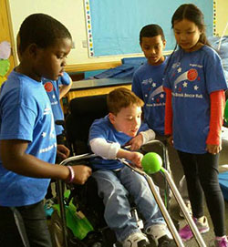 Cameron Weatherford gets encouragement from fellow students Isaiah Robinson and Violet Ottenwess as he launches his bocce ball from a special device