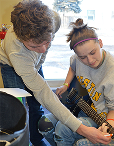 Volunteer Harrison Rice, a South Christian High School student, teaches Kelloggsville sophomore Tye Ward to play the guitar