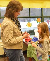 Camp Blodgett Program Director Susan Doughty shows Pine Island Elementary fourth grade student Jadelyn Hall how to make a bracelet