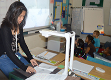 Janet Vu reads a story to second graders as they watch the illustrations on the projector