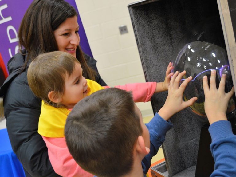 First-grader Wesley Reinholtz and his sister, Hallie, getting a boost from mom Erin, check out an electricity exhibit at the STEAM Museum