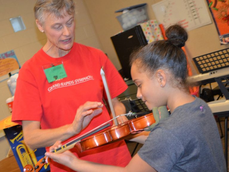Linda Nelson, violinist with the Grand Rapids Symphony, shows Meeah Fisher how to hold a bow