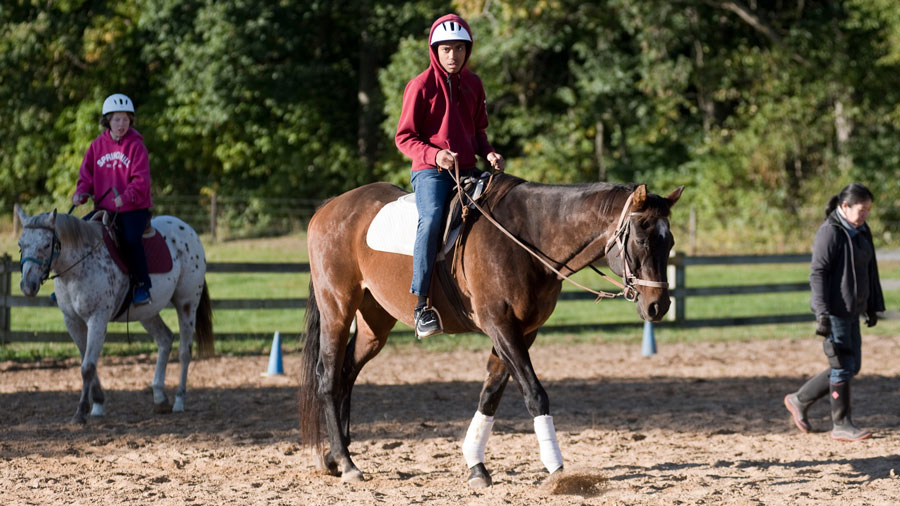 From left, seniors Kalie Triick and Ethan Bowerman walk their horses around the arena with an instructor at their side