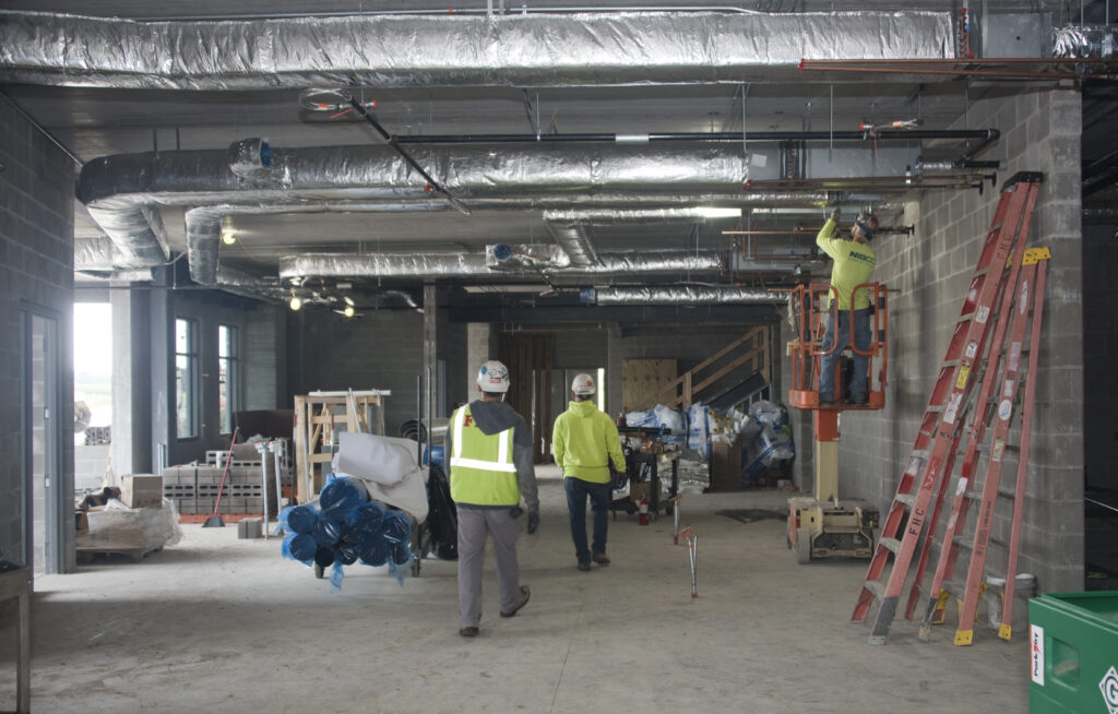 Construction workers install overhead hydronics heating and cooling systems inside the Cal Community Center 