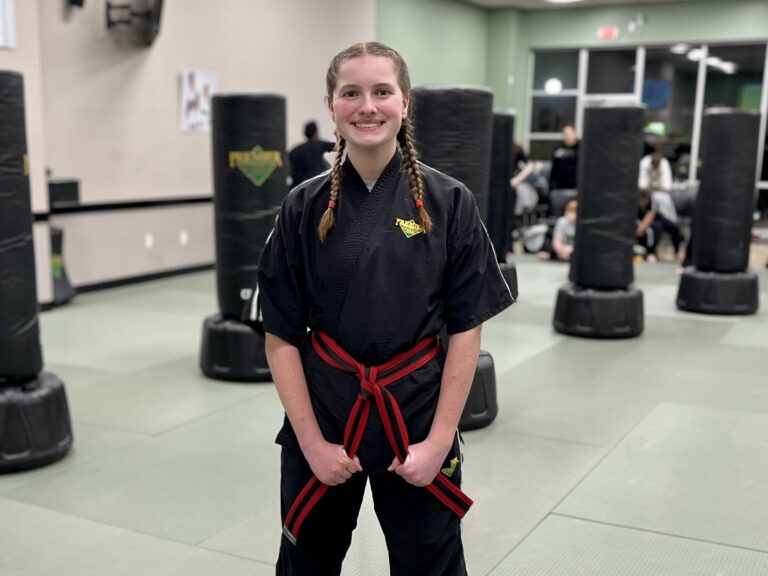 A young martial artist girl stands wearing her karate gi with red striped belt