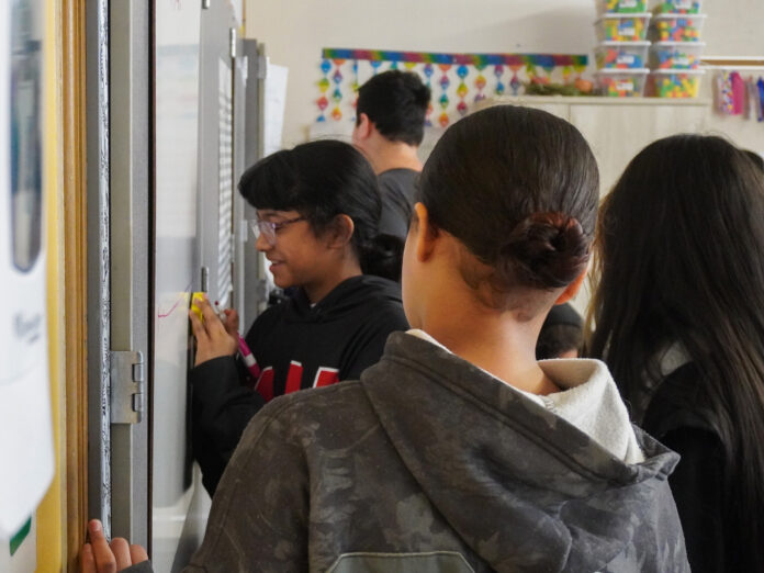 Student draws a number line on a white board to solve an equation with her group mates.