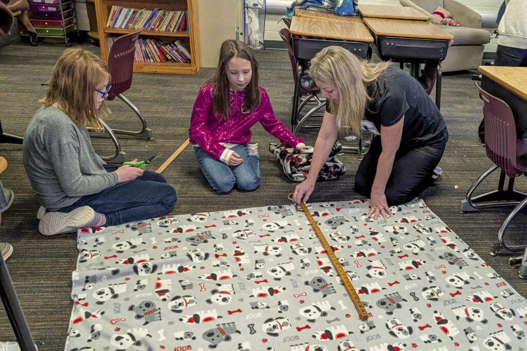 A woman helps two girls spread out fabric on the floor
