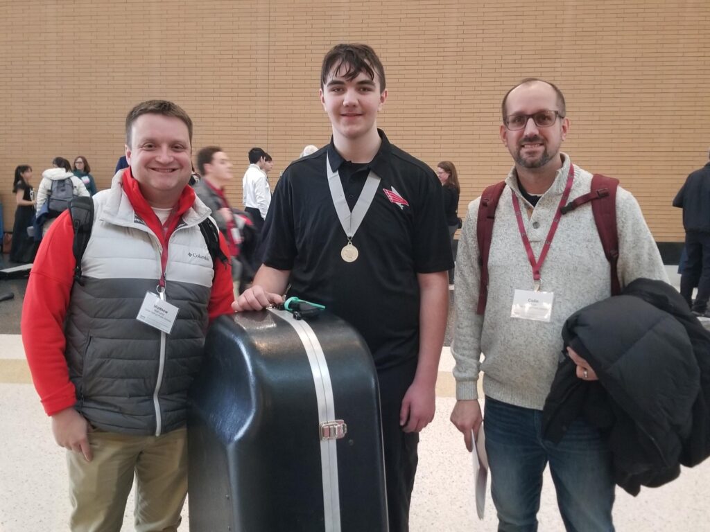 Two music teachers stand on either side of an eighth-grade student