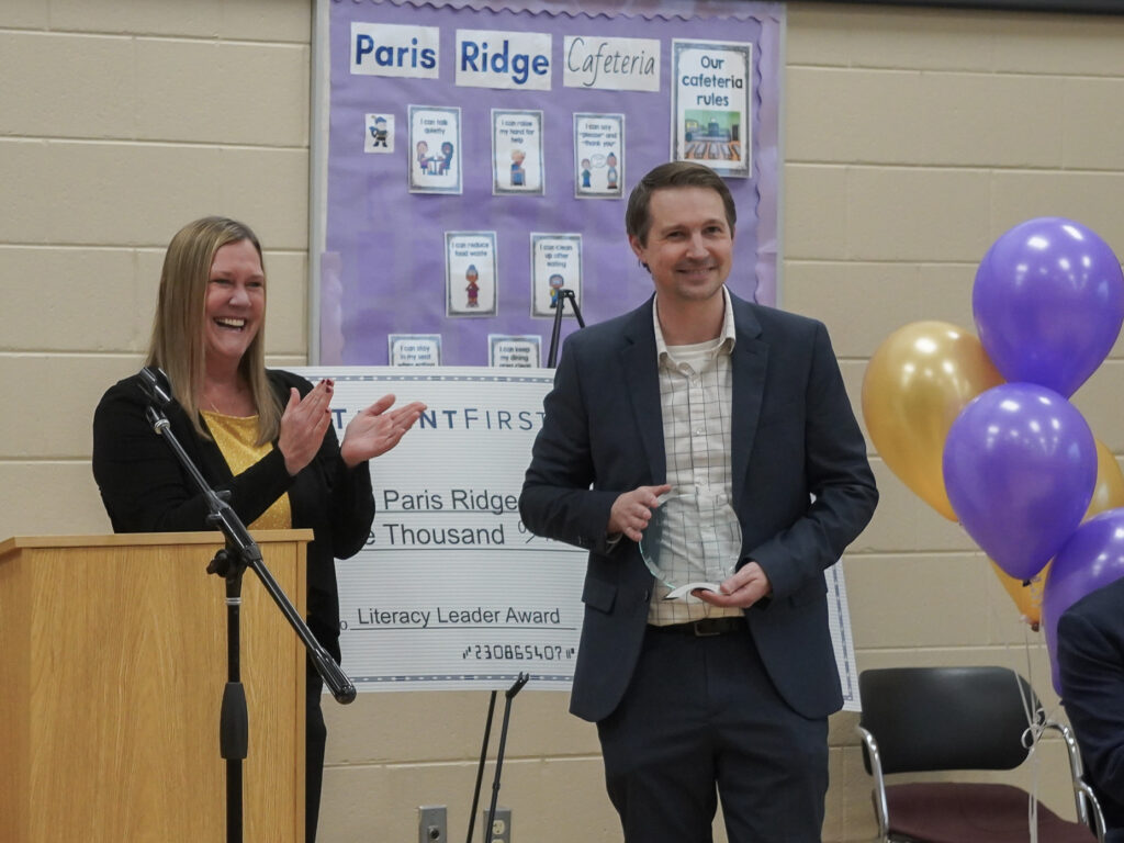 Woman and man smiling and clapping their hands to celebrate their students.