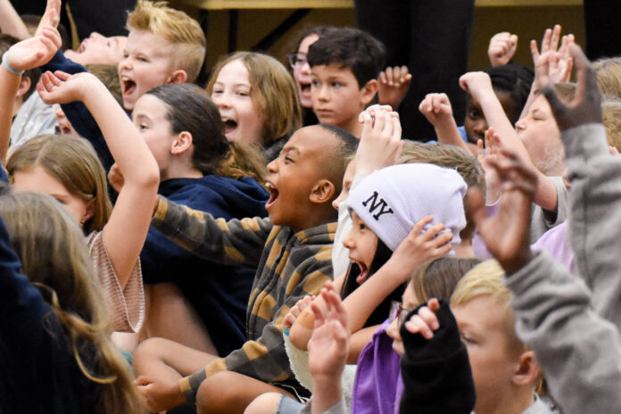 A group of students cheering, smiling and waving their hands in the air.