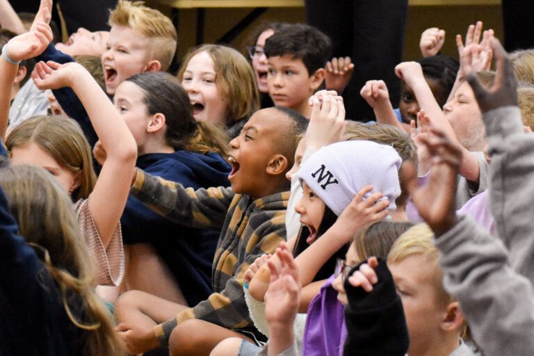 A group of students cheering, smiling and waving their hands in the air.