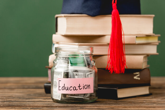 books, academic cap and piggy bank on wooden surface isolated on green